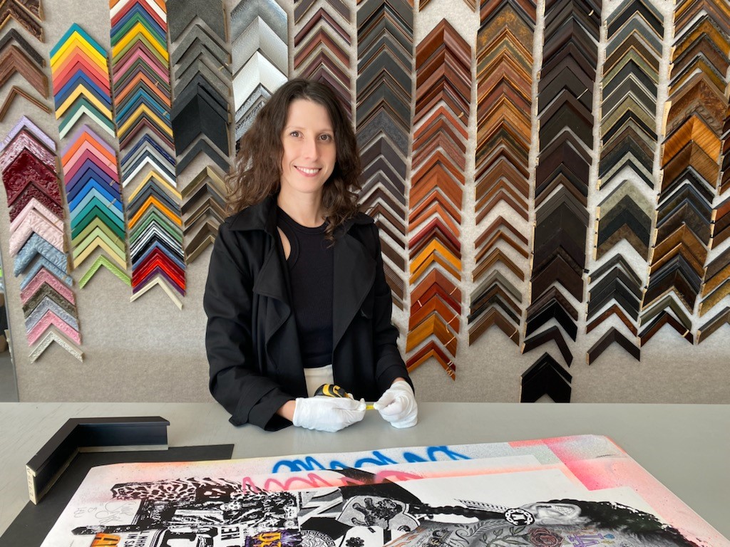 A lady stading in front of some colorful columns and her hand restig on a table with her artt